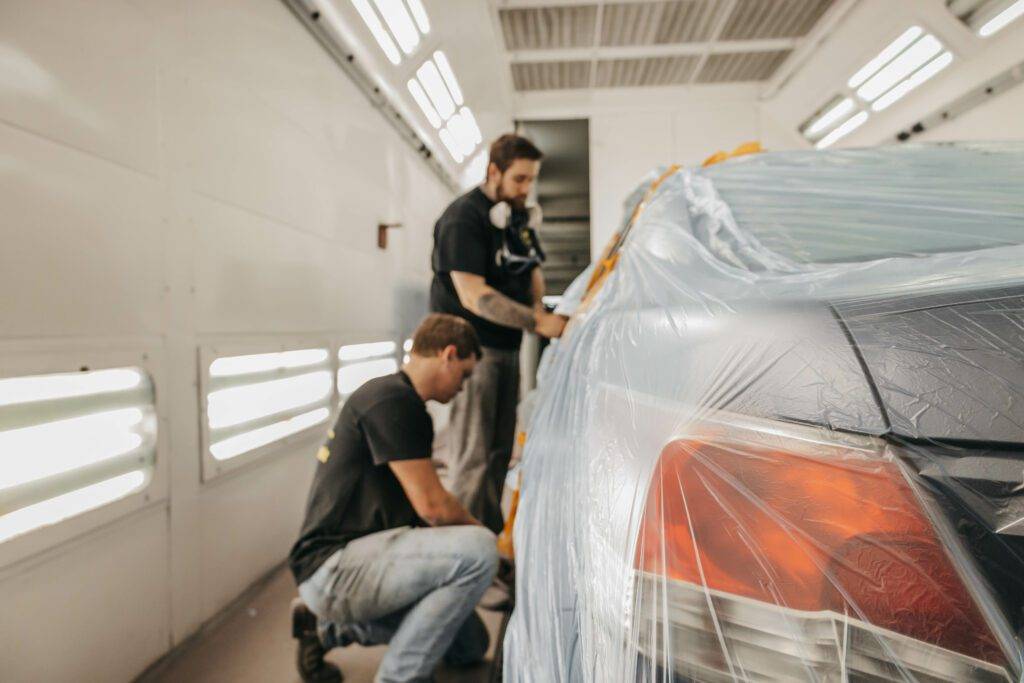 Two men repairing a car in a garage, focused on the engine and surrounded by tools and equipment