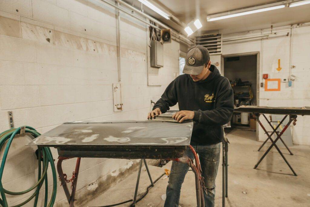 A man is focused on a project at a workbench in a garage, surrounded by tools and materials.