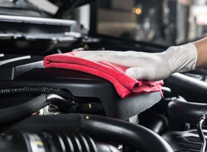 Gloved hand wiping a car engine with a red cloth, emphasizing cleanliness and care in automotive maintenance at Barry's Collision Repair.