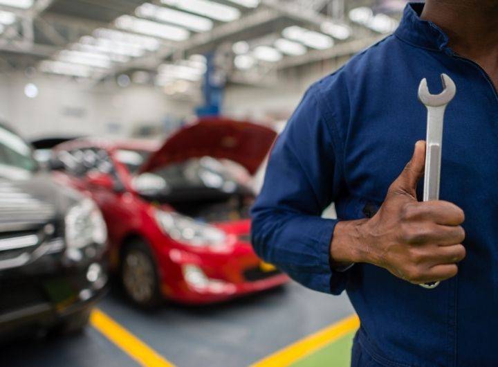 Mechanic in blue coveralls holds a wrench, standing in a brightly lit garage.