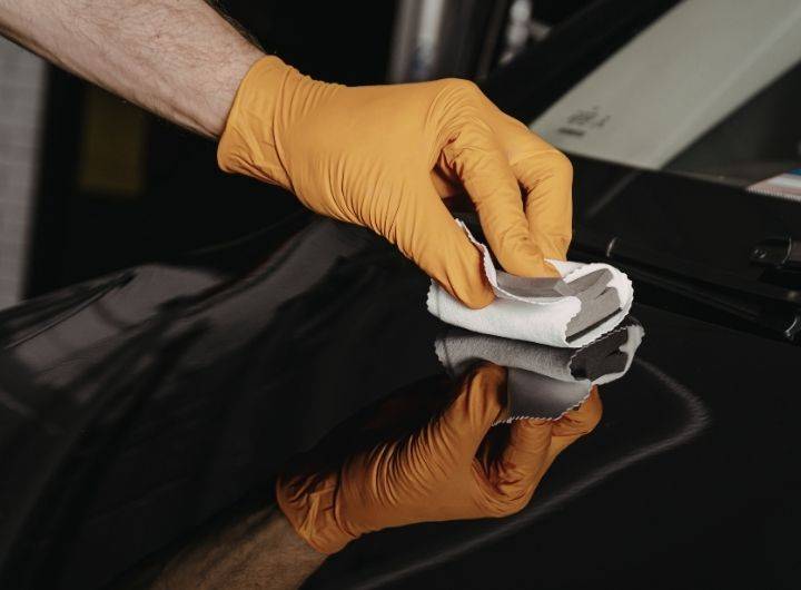 A person wearing an orange glove is cleaning the exterior of a car with a cloth.