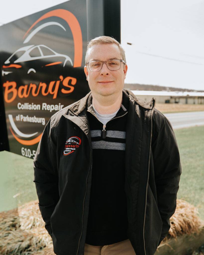 Ryan Will, Manager at Barry's Collision Repair, standing in front of the business sign, showcasing the commitment to quality automotive services.